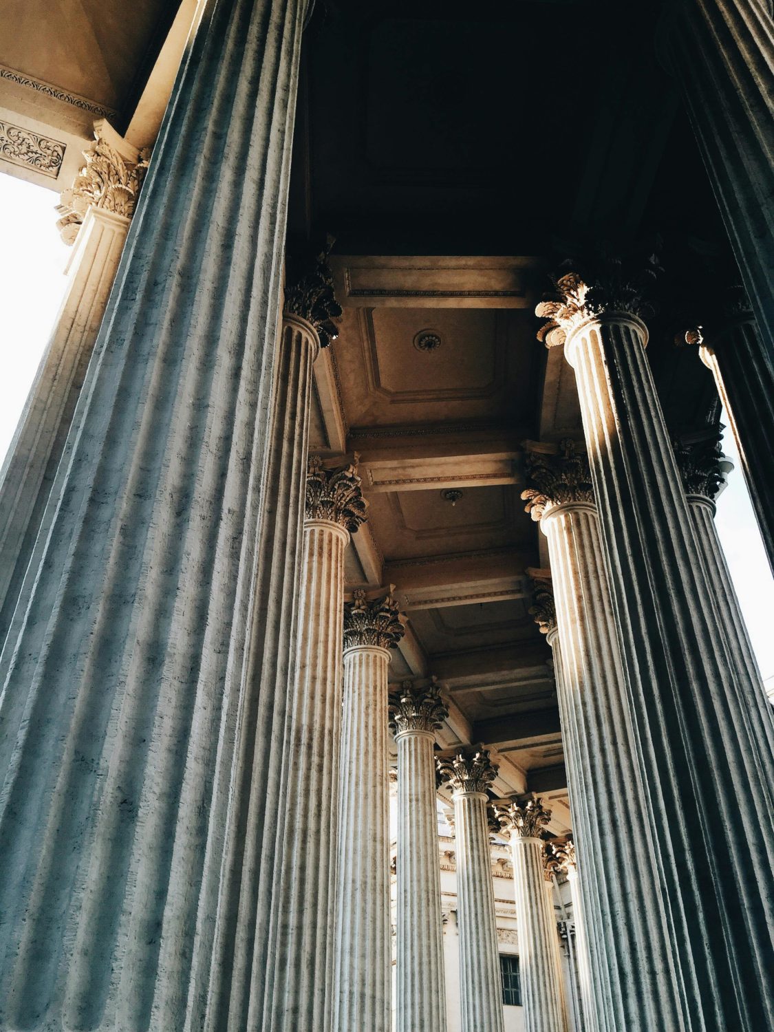 Dramatic upward shot of classic stone columns lit by sunlight with ornate details.