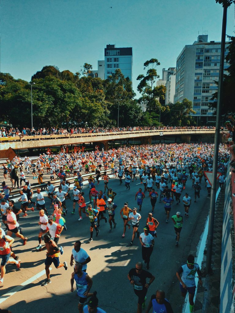 From above of crowd of sportive multiracial people in sportswear running near bridge in modern district on sunny day
